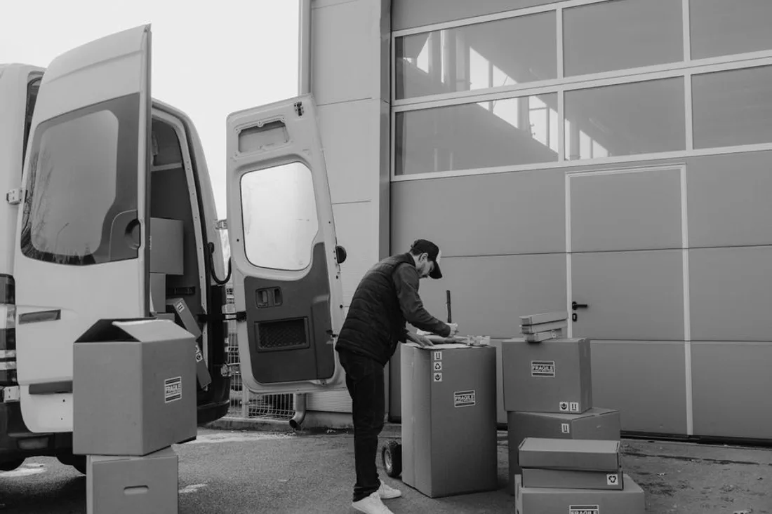Mitarbeiter beschriftet Umzugskartons neben zwei Transportern